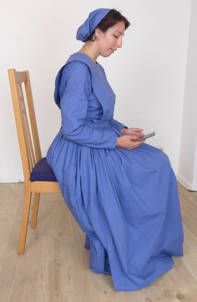 Woman in a plain cape dress, sitting on a chair, looking at her phone